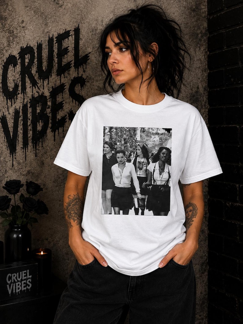 May include: A white short-sleeved t-shirt featuring a black and white rectangular graphic print on the chest. The graphic depicts four individuals standing together in a group. The shirt has a crew neckline and a standard fit, constructed from cotton fabric.