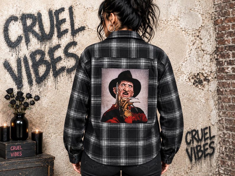 May include: A black and white plaid button-down shirt featuring a large rectangular graphic on the back. The graphic depicts a character wearing a brown fedora and a red and black striped sweater, with metallic clawed fingers raised near the face.