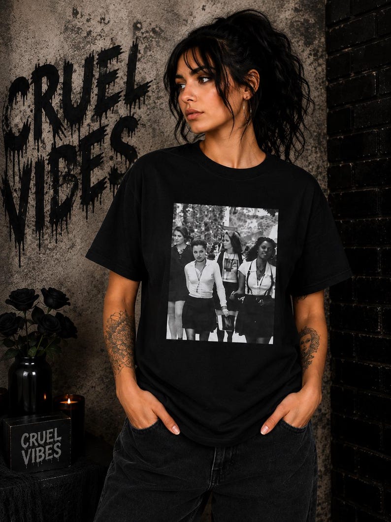 May include: A black short-sleeved t-shirt featuring a rectangular black and white photographic print on the chest. The graphic depicts four individuals in school-style attire, including button-down shirts, skirts, and suspenders, standing together.
