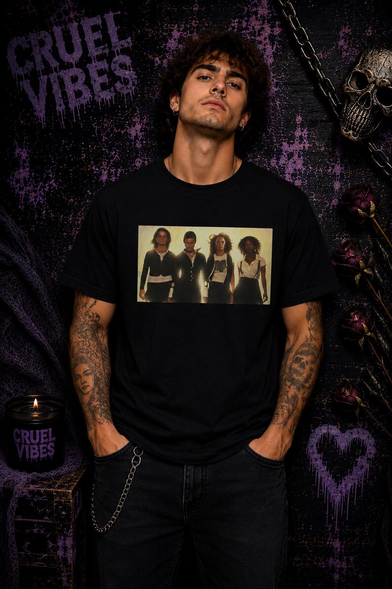 K&ouml;nnte beinhalten: Ein schwarzes T-Shirt mit kurzen &Auml;rmeln und einem rechteckigen Grafikdruck von vier Personen, die in einer Reihe stehen. Das Shirt besteht aus einfarbigem schwarzem Stoff und zeigt ein klares, zentriertes Foto der Gruppe auf der Brust.