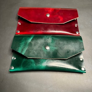 May include: Three leather wallets, one red, one green, and one brown. The green wallet has the letters "M71" embossed on the front.