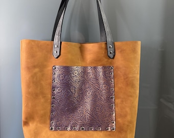 May include: A brown leather tote bag with black leather straps and a purple floral embossed leather pocket on the front.
