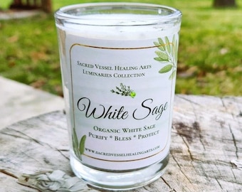 May include: A clear glass candle container with a white label featuring the text Sacred Vessel Healing Arts Luminaries Collection, White Sage, Organic White Sage, Purify Bless Protect, and a website URL, decorated with green leaf illustrations.