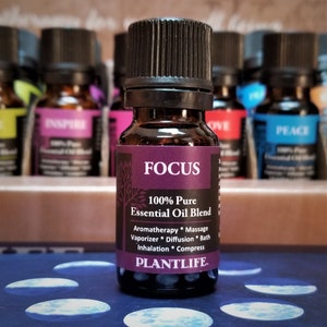 May include: A small brown glass bottle with a black cap and label. The label says "FOCUS 100% Pure Essential Oil Blend" and lists uses for aromatherapy, massage, vaporizer, diffusion, bath, inhalation, and compress. The label also says "PLANTLIFE".