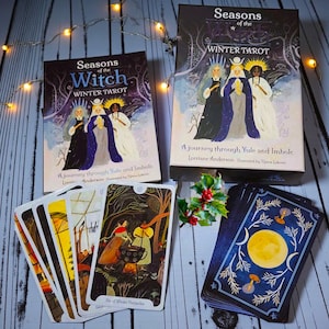 May include: A tarot card set titled "Seasons of the Witch Winter Tarot" with a box and a deck of cards. The box features illustrations of three figures in robes. The cards show detailed artwork with a winter theme. The text "A journey through Yule and Imbolc" is visible.
