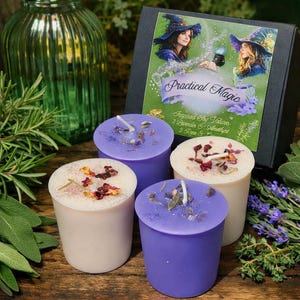 May include: A set of four soy votive candles in a black box labeled Practical Magic. Two candles are light purple with amethyst crystals and two are off-white with dried flower petals. Each candle features a central wick and botanical accents.