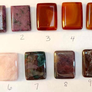 May include: Nine rectangular gemstones in various colors, including pink, red, brown, and green. Each stone is polished and has a smooth surface. Numbers 1 through 9 are written below each stone.