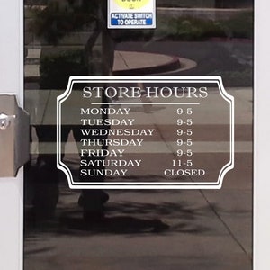 May include: A glass door with a white frame displays store hours. The hours are listed in white text on a decorative sign. The store is open Monday through Friday from 9 AM to 5 PM, Saturday from 11 AM to 5 PM, and closed on Sunday.