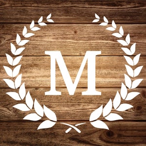 May include: White letter M surrounded by a white laurel wreath on a brown wood background.