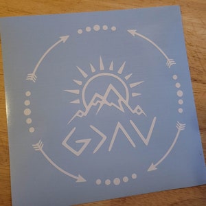 May include: White vinyl decal with a mountain range, sun, and the text "God > All" in a circle with arrows and dots.