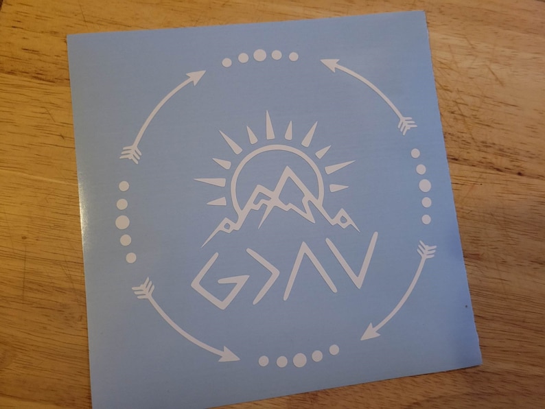 May include: White vinyl decal with a mountain range, sun, and the text "God > All" in a circle with arrows and dots.