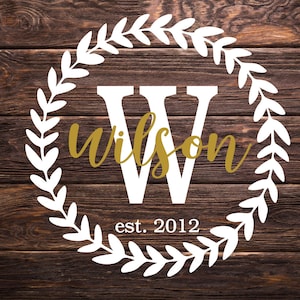 May include: White wreath with a large white letter W in the center. The word "Wilson" is written in gold script inside the wreath. The text "est. 2012" is written below the wreath.