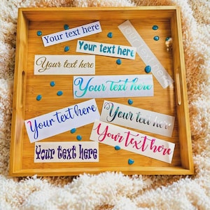 May include: A square bamboo serving tray containing multiple rectangular adhesive labels, each featuring the phrase Your text here in various colors, including blue, teal, gold, purple, pink, and silver, scattered with small blue beads.
