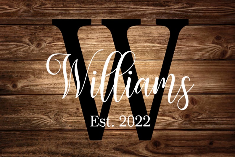 May include: A black wooden sign with the last name "Williams" written in white cursive script. The letter "W" is large and in block letters. The text "Est. 2022" is written below the name.