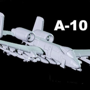 May include: A white model of an A-10 Warthog aircraft with a detailed design and multiple weapons attached to the underside.