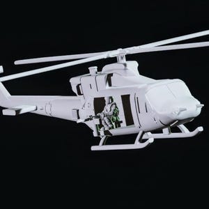 May include: A white model helicopter with a pilot figure in the cockpit. The helicopter has a black interior and a clear canopy.