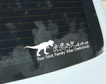 May include: White vinyl car decal featuring a Tyrannosaurus Rex chasing a stick figure family. The text "Your Stick Family Was Delicious" is below the figures. The decal is applied to a car window.
