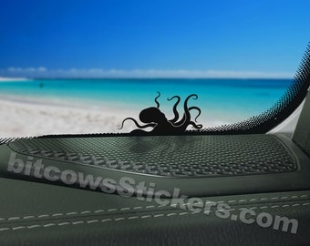 May include: Black octopus silhouette sticker on a car window with a beach scene in the background. The sticker is placed on a black speaker grille. The text "bitcowsstickers.com" is visible in the lower right corner.