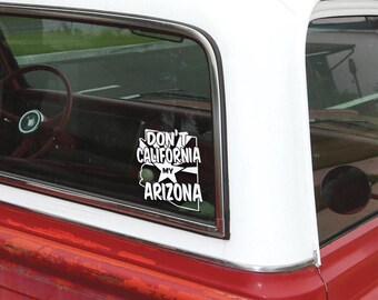 May include: A white vinyl sticker with the text "Don't California My Arizona" in black lettering. The sticker is on the back window of a red pickup truck.