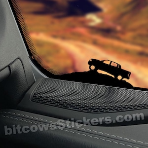 以下が含まれることがあります： 夕焼けの背景に、丘を登るピックアップトラックの黒いシルエット。トラックは車の窓にあり、その下に黒いスピーカーグリルがあります。右下隅に「bitcowsStickers.com」というテキストが表示されています。