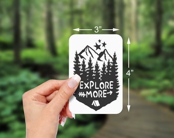 Könnte beinhalten: Schwarz-weißer Aufkleber mit einer Bergkette, Kiefern, Sternen und dem Text "Explore More" mit einem Pfeil nach rechts. Der Aufkleber ist 7,6 cm breit und 10,2 cm hoch.