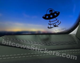 May include: Black vinyl sticker featuring a cartoon UFO with an alien and a person being abducted. The UFO is black with blue accents. The sticker is applied to a car window, with the website bitcowsStickers.com visible.