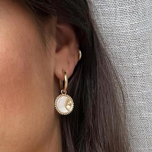 May include: Gold hoop earrings with a white and gold moon charm pendant.