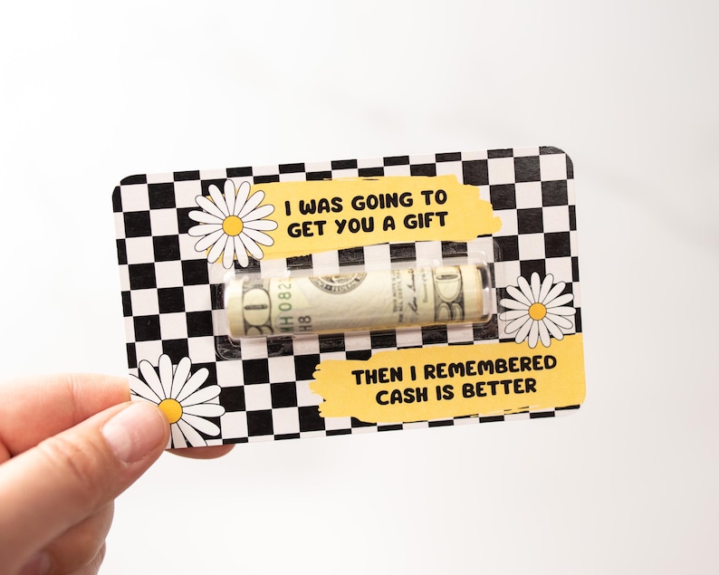 Puede incluir: Una tarjeta a cuadros en blanco y negro con un dise&ntilde;o de margarita amarilla. La tarjeta tiene una ventana de pl&aacute;stico transparente que muestra un billete de d&oacute;lar enrollado. El texto en la tarjeta dice "Iba a darte un regalo, pero luego record&eacute; que el efectivo es mejor."