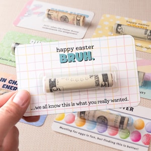 May include: A colorful card with the text "happy easter BRUH." and a rolled up $5 bill inside a plastic sleeve. The card is surrounded by other cards with similar designs.