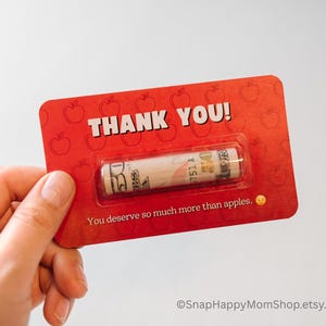 May include: Red card with a rolled up dollar bill inside. The card has a red apple pattern and the text "THANK YOU! You deserve so much more than apples."