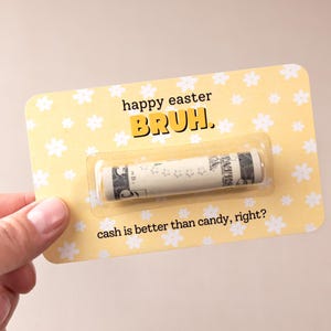 May include: A yellow card with white flowers printed on it. The card says "happy easter bruh." and "cash is better than candy, right?" There is a rolled up dollar bill inside a clear plastic sleeve on the card.