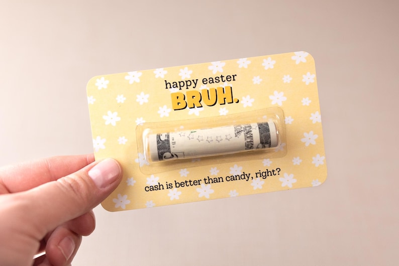 May include: A yellow card with white flowers printed on it. The card says "happy easter bruh." and "cash is better than candy, right?" There is a rolled up dollar bill inside a clear plastic sleeve on the card.