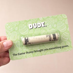 May include: A green card with a white Easter egg pattern and the text "DUDE." A rolled up dollar bill is inside a clear plastic sleeve. The text "The Easter Bunny brought you something green." is printed below the dollar bill.
