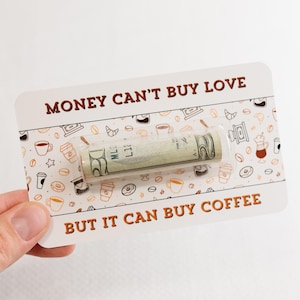 Puede incluir: Una tarjeta blanca con texto marr&oacute;n que dice "El dinero no puede comprar el amor pero puede comprar caf&eacute;." Un billete de d&oacute;lar enrollado es visible a trav&eacute;s de una ventana de pl&aacute;stico transparente en la tarjeta. La tarjeta est&aacute; decorada con un patr&oacute;n de tazas de caf&eacute;, donuts y estrellas.