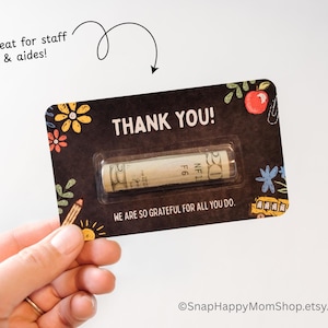 May include: A black and white card with the text "THANK YOU!" and a small rolled up bill of money inside a clear plastic sleeve. The card has a chalkboard background with colorful drawings of school supplies and the text "WE ARE SO GRATEFUL FOR ALL YOU DO."