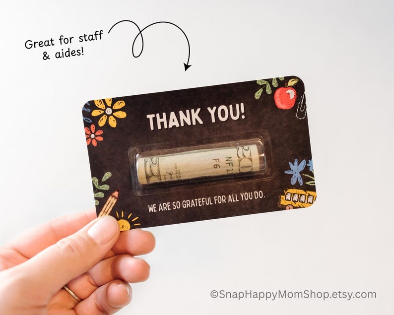 May include: A black and white card with the text "THANK YOU!" and a small rolled up bill of money inside a clear plastic sleeve. The card has a chalkboard background with colorful drawings of school supplies and the text "WE ARE SO GRATEFUL FOR ALL YOU DO."
