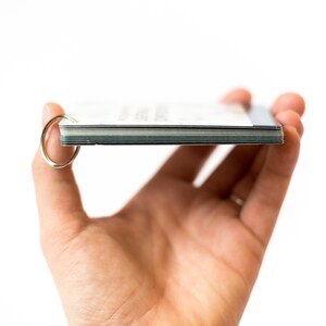 May include: A stack of cards with rounded corners held in a hand. The cards are bound together with a silver ring.