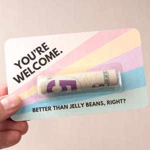 May include: A colorful card with the text "You're Welcome." and a rolled up $5 bill inside a clear plastic window. The text "Better than jelly beans, right?" is printed below the window.