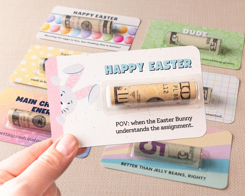 May include: A set of colorful Easter cards with a bunny rabbit illustration and the text "Happy Easter". Each card features a rolled-up dollar bill inside a clear plastic sleeve. The text "POV: when the Easter Bunny understands the assignment." is printed on one of the cards.