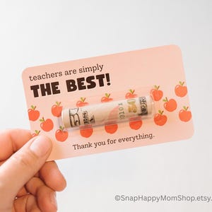 May include: A pink card with a red apple pattern and the text "teachers are simply THE BEST!"  A rolled up $50 bill is inside a clear plastic sleeve on the card. The text "Thank you for everything." is below the bill.