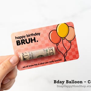 Może przedstawiać: Prostokątna karta w kolorze koralowym w kratkę, z trzema balonami oraz napisem "happy birthday BRUH." i "...we all know this is what you really wanted." Przezroczysta plastikowa kapsuła zawiera zwinięty banknot pięćdziesięciodolarowy.