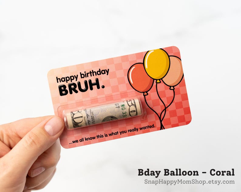 Może przedstawiać: Prostokątna karta w kolorze koralowym w kratkę, z trzema balonami oraz napisem "happy birthday BRUH." i "...we all know this is what you really wanted." Przezroczysta plastikowa kapsuła zawiera zwinięty banknot pięćdziesięciodolarowy.