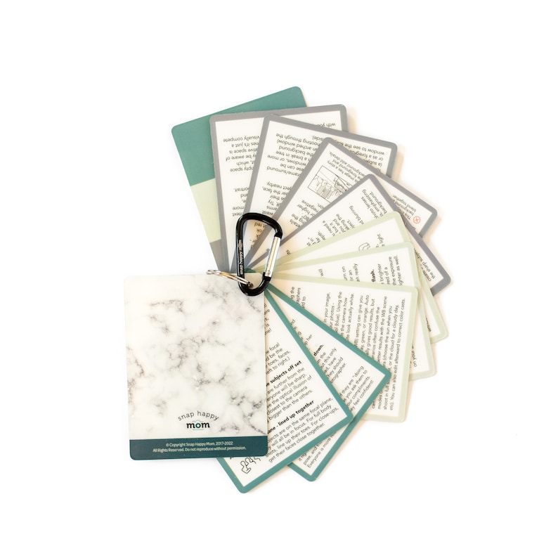 May include: A set of green and white cards with a marble-patterned card on top. The cards have text on them and are held together by a black carabiner clip. The text on the marble card reads "snap happy mom".