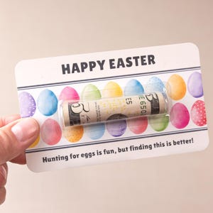 May include: A white card with the words "HAPPY EASTER" printed in black. The card has a row of colorful Easter eggs printed on it. A rolled up dollar bill is tucked inside the card.
