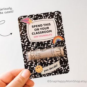 May include: A black and white notebook-style card with the text "Spend this on your classroom (or yourself!)" and a rolled-up dollar bill inside. The card has a rainbow sticker and a smiley face sticker.