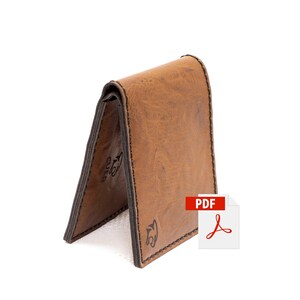 Puede incluir: Una cartera de cuero marrón con un borde cosido y un pequeño logotipo en la parte delantera. La cartera está doblada por la mitad y de pie. La imagen también incluye un icono PDF.