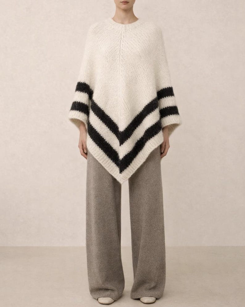 Pu&ograve; includere: Un poncho in maglia color crema con orlo a V e due strisce orizzontali nere vicino al bordo inferiore. Il capo &egrave; abbinato a pantaloni a gamba larga color tortora m&eacute;lange che arrivano fino a terra, creando un insieme dalla texture definita.