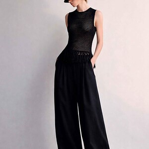May include: A black outfit consisting of a sleeveless, open-weave top with fringe detail, wide-leg pants, and a matching bucket hat. The outfit is all black and appears to be made of a lightweight material.