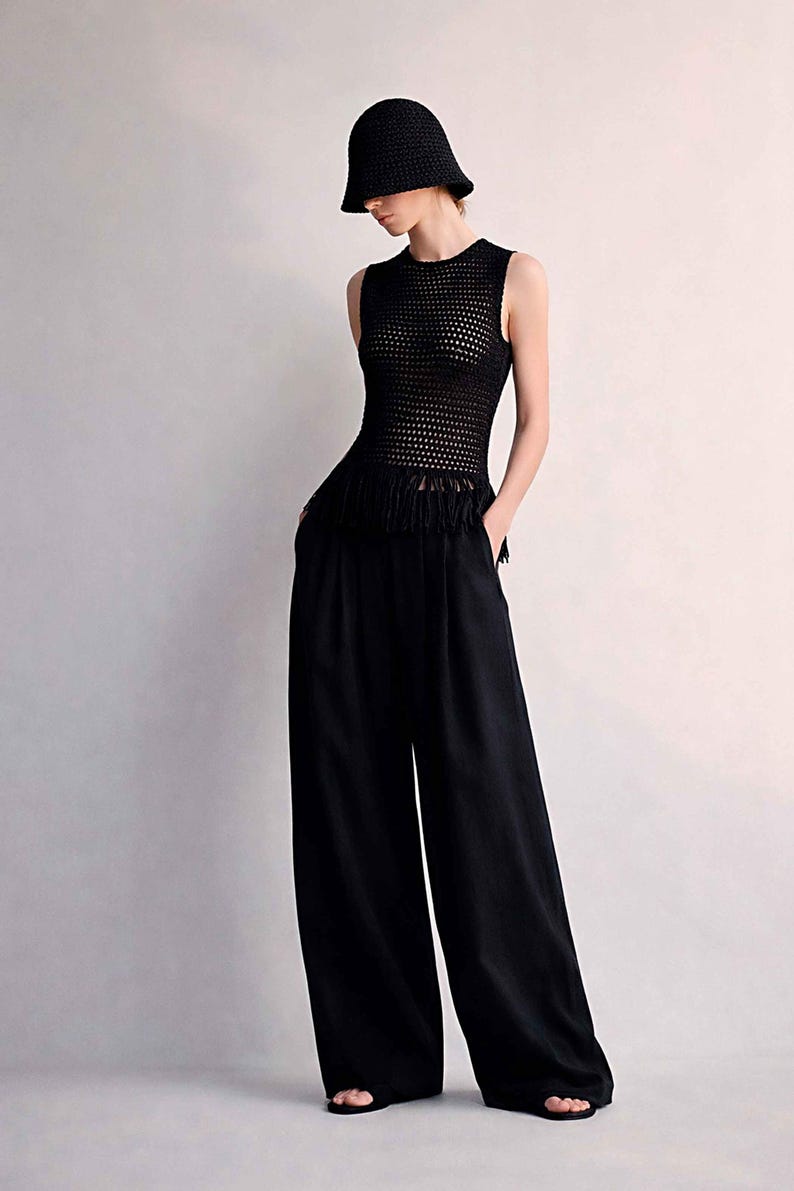 May include: A black outfit consisting of a sleeveless, open-weave top with fringe detail, wide-leg pants, and a matching bucket hat. The outfit is all black and appears to be made of a lightweight material.
