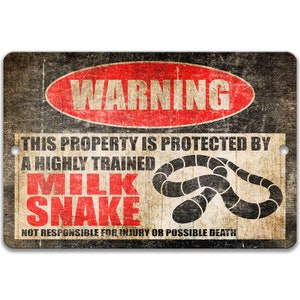 May include: A warning sign with a red circle and the word "WARNING" in white letters. The sign reads "This property is protected by a highly trained milk snake. Not responsible for injury or possible death." The sign has a distressed, vintage look.